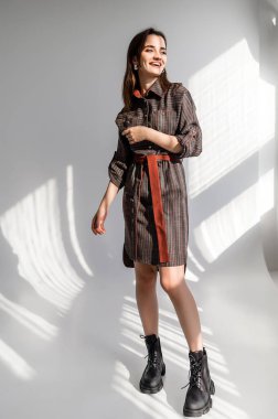 Beyaz arka planda gri kareli elbiseli çekici kahverengi saçlı kadın. Bir giyim kataloğu için fotoğraf çekinme