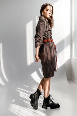 Beyaz arka planda gri kareli elbiseli çekici kahverengi saçlı kadın. Bir giyim kataloğu için fotoğraf çekinme