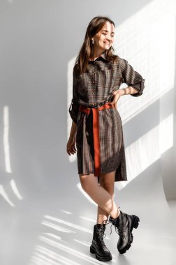 Beyaz arka planda gri kareli elbiseli çekici kahverengi saçlı kadın. Bir giyim kataloğu için fotoğraf çekinme