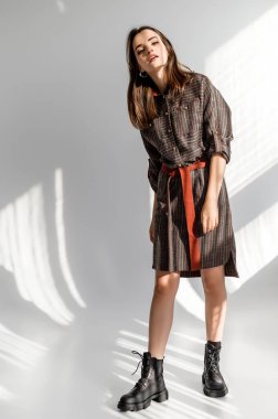 Beyaz arka planda gri kareli elbiseli çekici kahverengi saçlı kadın. Bir giyim kataloğu için fotoğraf çekinme