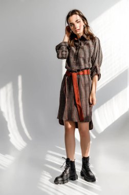 Beyaz arka planda gri kareli elbiseli çekici kahverengi saçlı kadın. Bir giyim kataloğu için fotoğraf çekinme