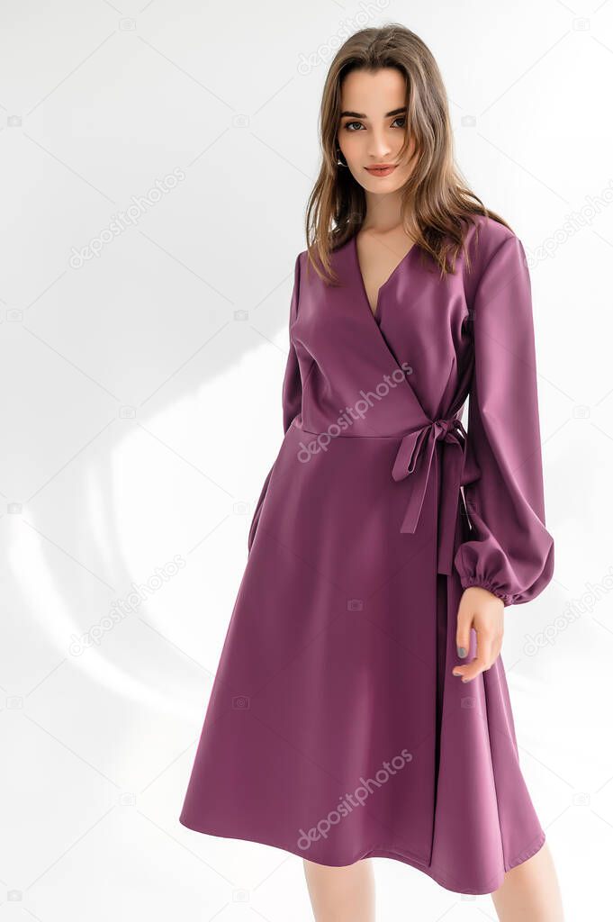 Attractive brown-haired woman in a purple checkered dress on a white background. Photosession for a clothing catalog
