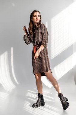 Beyaz arka planda gri kareli elbiseli çekici kahverengi saçlı kadın. Bir giyim kataloğu için fotoğraf çekinme