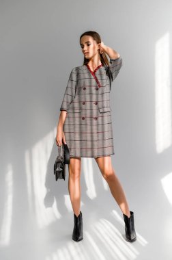 Beyaz arka planda gri kareli elbiseli çekici kahverengi saçlı kadın. Bir giyim kataloğu için fotoğraf çekinme