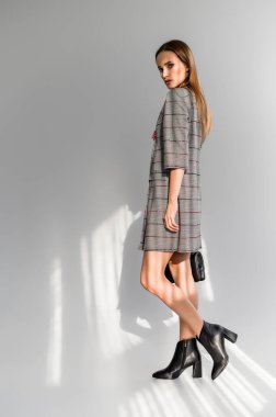 Beyaz arka planda gri kareli elbiseli çekici kahverengi saçlı kadın. Bir giyim kataloğu için fotoğraf çekinme