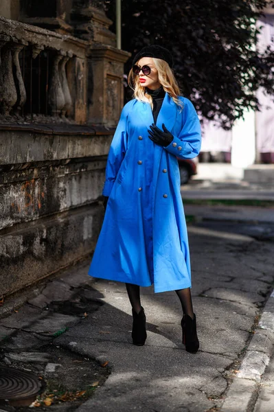 Fashionable model in a blue cloak posing near old wall