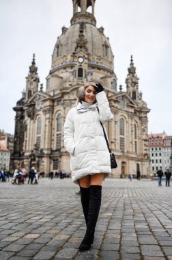 Beyaz ceketli bir sarışın eski şehirde yürüyor.