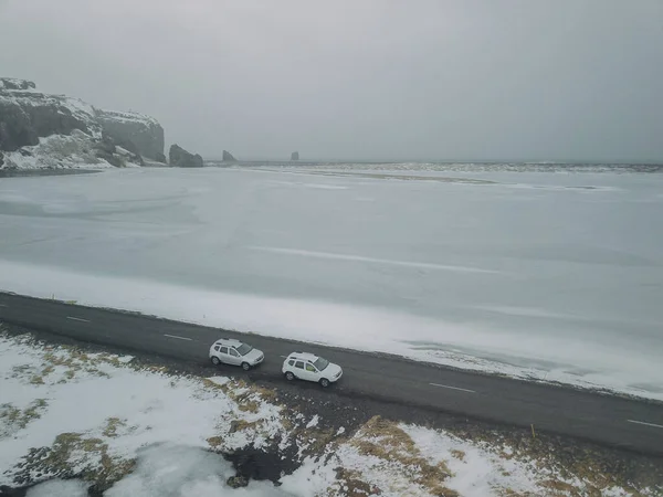 Un coche está conduciendo en el camino polvoriento a lo largo de pastizales con cordillera de nieve y fondo de cielo brillante — Foto de Stock