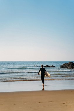 Mayolu dalgın bir adam sörf tahtasıyla suya giriyor.