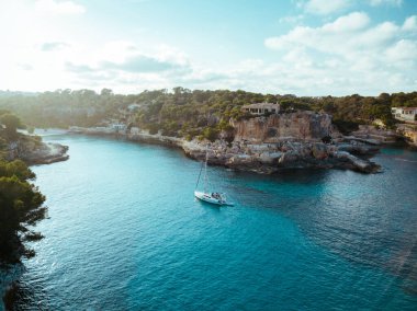 İHA panoramik görüntüsü parlak mavi körfezde demirlemiş yatlar Cala Blanca Andratx, Palma de Mallorca, kayalık sahil manzarası, Balear Adaları İspanya.