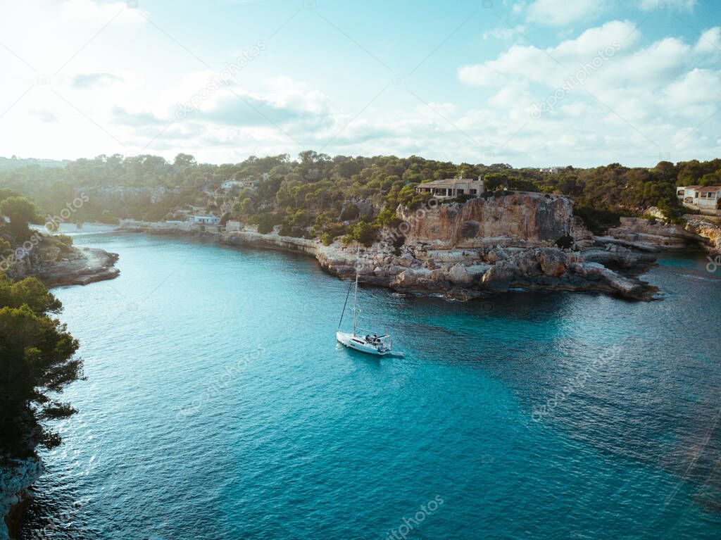 Drone panoramic image moored yachts on bright blue bay Cala Blanca Andratx, Palma de Mallorca, rocky coast breathtaking view, Balearic Islands Spain.