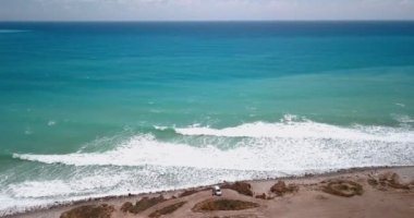 Mavi deniz manzarası ve yoldan geçen beyaz kumsal arabaları.