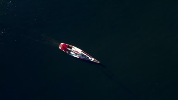 Top down drone tiro de um iate navegando através do oceano azul profundo com a luz ondulante embaixo — Vídeo de Stock
