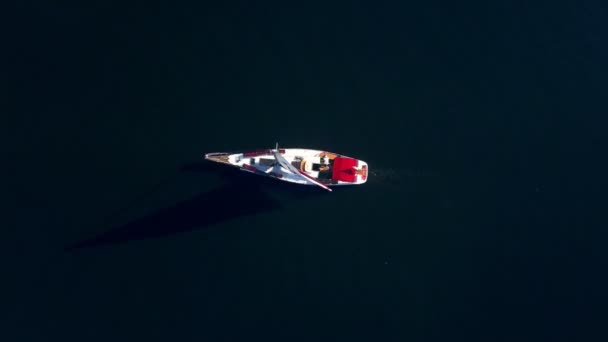 Top down drone shot van een jacht zeilen door de diepblauwe oceaan met het kabbelende licht eronder — Stockvideo