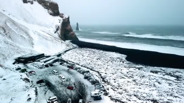Luchtfoto van een parkeerplaats in de buurt van een zwart vulkanisch strand in IJsland en een trol tenen kliffen in de zee. — Stockvideo