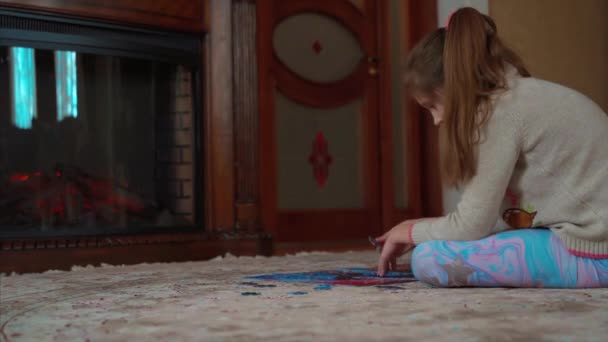 Little girl sits at home by the fireplace and collects puzzles — Stock Video