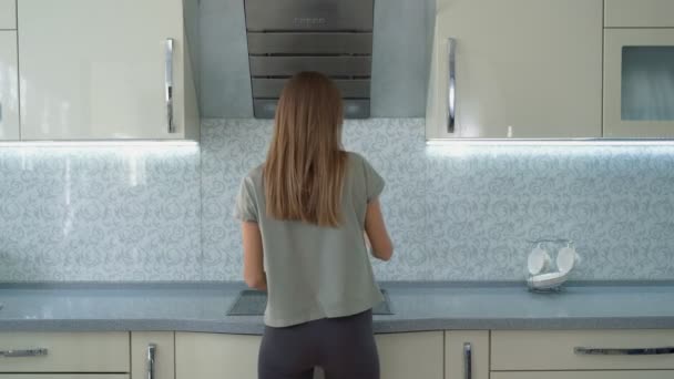 Roztomilá holka vařící polévku na sporáku v kuchyni. Otočte se a mladá žena ochutnává polévku na lžíci v moderní kuchyni — Stock video
