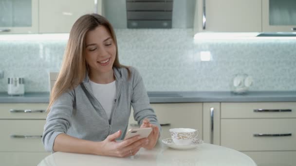 Jong meisje is typen op smartphone zitten in de keuken — Stockvideo