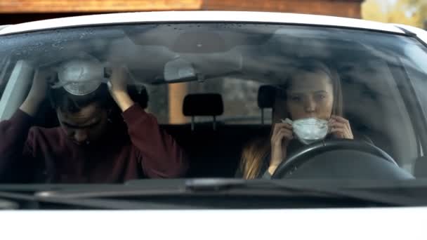 Una chica y un chico usan máscaras del virus sentado en el coche, la vista desde el parabrisas del coche . — Vídeos de Stock