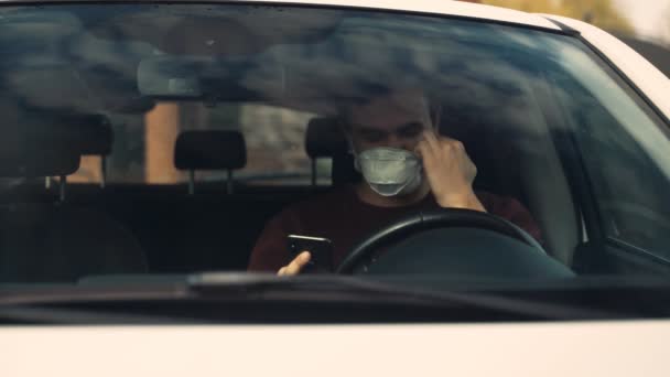 Un joven habla por video sentado en el coche, quitándose la máscara para hablar . — Vídeos de Stock