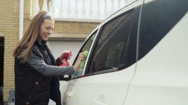 Молода жінка миє лобове скло автомобіля зі скрипом на відкритому повітрі . — стокове відео
