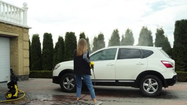 Μια χαριτωμένη γυναίκα πλένει ένα λευκό αυτοκίνητο στο δρόμο — Αρχείο Βίντεο