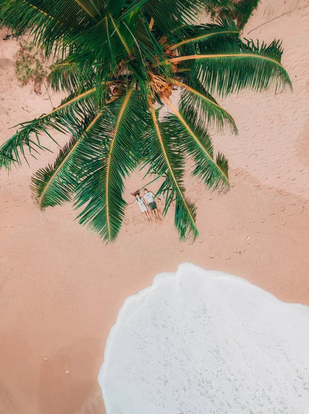 Vista aérea de una joven pareja acostada en la playa bajo una palmera. El océano los abraza, la vista desde el dron . Fotos De Stock Sin Royalties Gratis