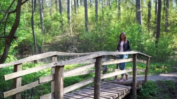 Mujeres jóvenes camina en máscara médica en un puente de madera en un parque o bosque — Vídeo de stock