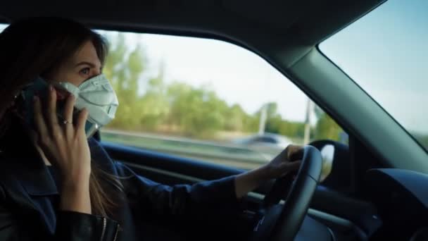 Joven mujer de negocios sentada en un coche, hablando por teléfono con una máscara médica — Vídeo de stock