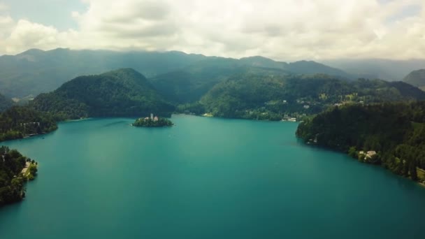 Sjön Bled ö kyrka och båtar i vinterlandskapet. Lugnt sjövatten speglar himlen moln ovan, snötäckta berg i bakgrunden — Stockvideo