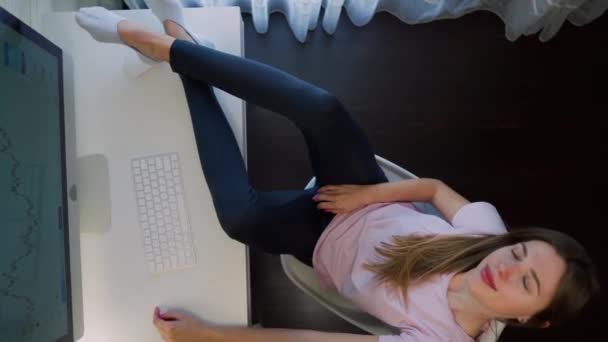 疲れている女の子は、コンピュータに座って、テーブルの上に足を置く。上からの眺め。家にいて — ストック動画