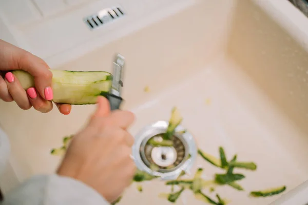 Mujer limpia pepino en el fregadero en la cocina Imagen De Stock