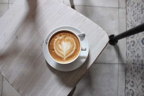 Coffee. Cup of freshly brewed Cappuccino Coffee with latte art, heart pattern. Morning coffee in the cafe. One Cup of coffee over white wooden chair. Enjoying the little things.