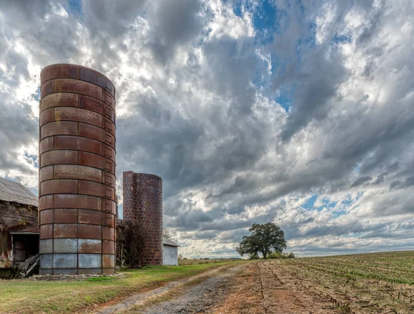 Stodola se dvěma sily na farmě pod bouřlivou oblohou se stromem v — Stock fotografie