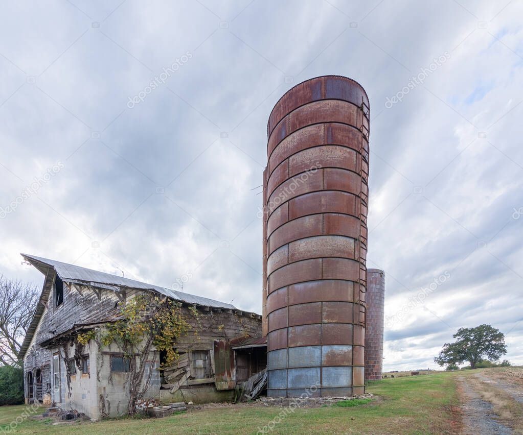 Abandoned barn with silo under stormy clouds