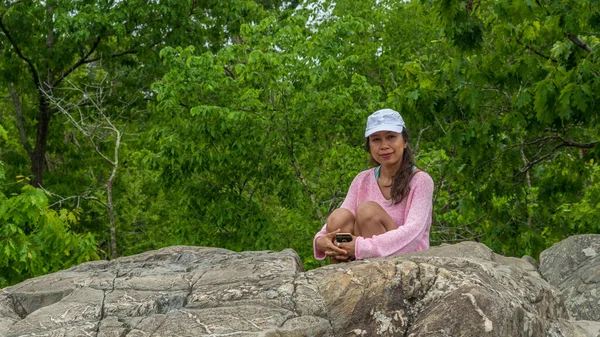 Asian woman sitting on large rock with forest in background