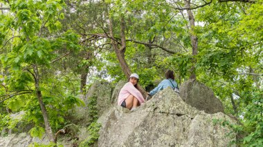 Pembe kazaklı, şapkalı ve kızı ormandaki kayalık kayalıklarda oturuyor.