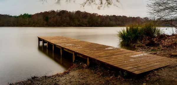 Doca de madeira vazia que leva a um lago liso — Fotografia de Stock