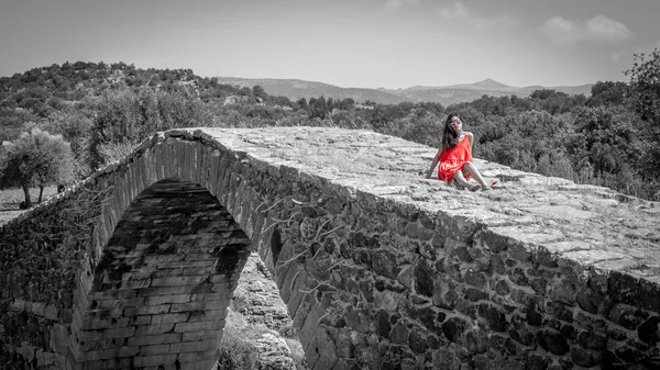 Adolescente chica en vestido rojo sentado en el puente antiguo — Foto de Stock