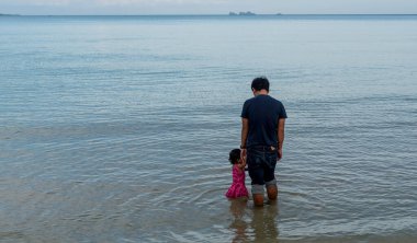 Baba ve kızı Tayland Körfezi 'nde arka planda adayla birlikte sığ sularda duruyor.
