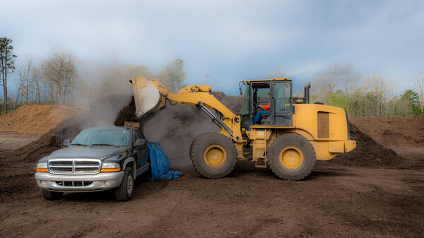 Front end loader dropping load of mulch onto bed of black pickup truck at the dump in Orange County, North Carolina