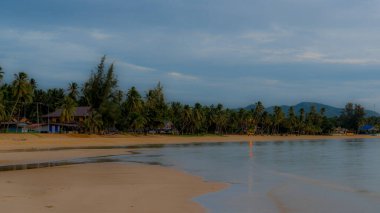 Gün batımında sahilde güzel bir Tayland köyü. Dalgalar alçaldığında etrafları palmiye ağaçlarıyla çevrili.