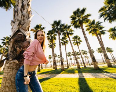 palmiye ağaçları ve günbatımı bir arka plan üzerinde mutlu genç gülümseyen kadın güneş sahiptir ve kameraya benziyor