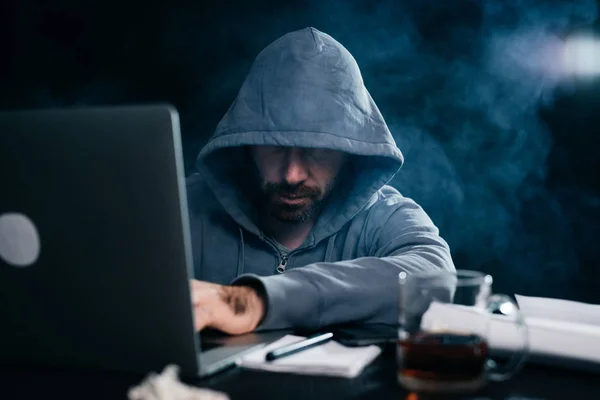 A computer hacker is typing on a laptop in a smoky room. Dark background