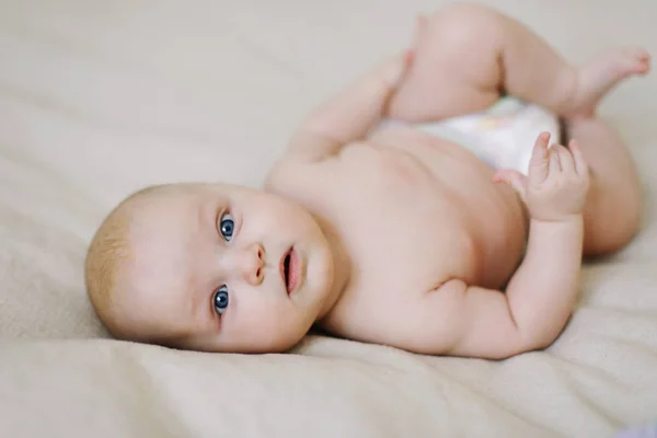 Divertente bambino che indossa un pannolino sdraiato su una coperta di maglia bianca. Cambio pannolino per bambini e cura della pelle . — Foto Stock