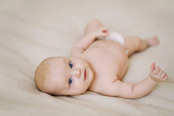 Funny little baby wearing a diaper lying on a white knitted blanket. Child nappy change and skin care. — Stock Photo, Image