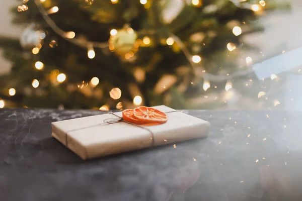 Karácsonyi kézműves papír ajándék díszített szárított narancs szeletek közelében karácsonyfa. Újévi dekoráció. lapos fektetés — Stock Fotó
