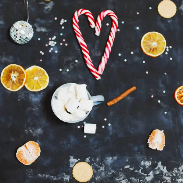 Świąteczna kompozycja. Przytulny kubek z piankami, laski cukierki, pomarańcze i dekoracje na czarnym tle. widok z góry — Zdjęcie stockowe