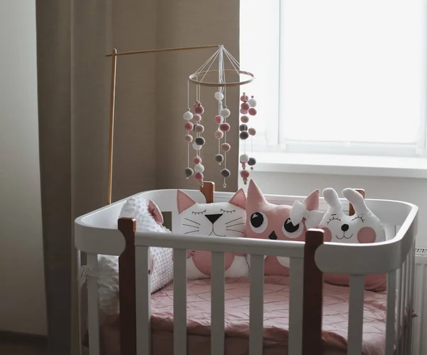 Hermoso interior de la habitación del bebé con una cuna. Cuna blanca con almohadas y manta rosa en la habitación del bebé. ropa de cama de color rosa pastel —  Fotos de Stock