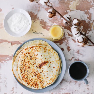 Stack of delicious homemade pancakes on plate with honey, sour cream and tea. Breakfast. Rustic style, close up top view. Flat lay